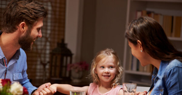 Kleines Mädchen hält ihre Eltern an den Händen am Abendessen, am Tisch sitzend