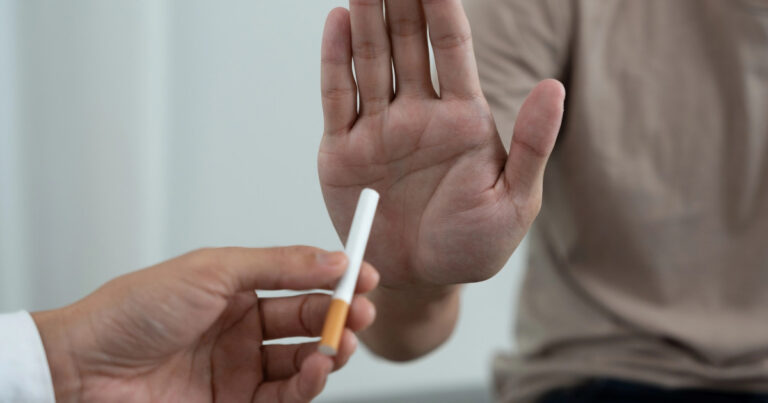 Eine Person bietet einer anderen Person eine Zigarette an, welche ablehnt mit einer Handgeste