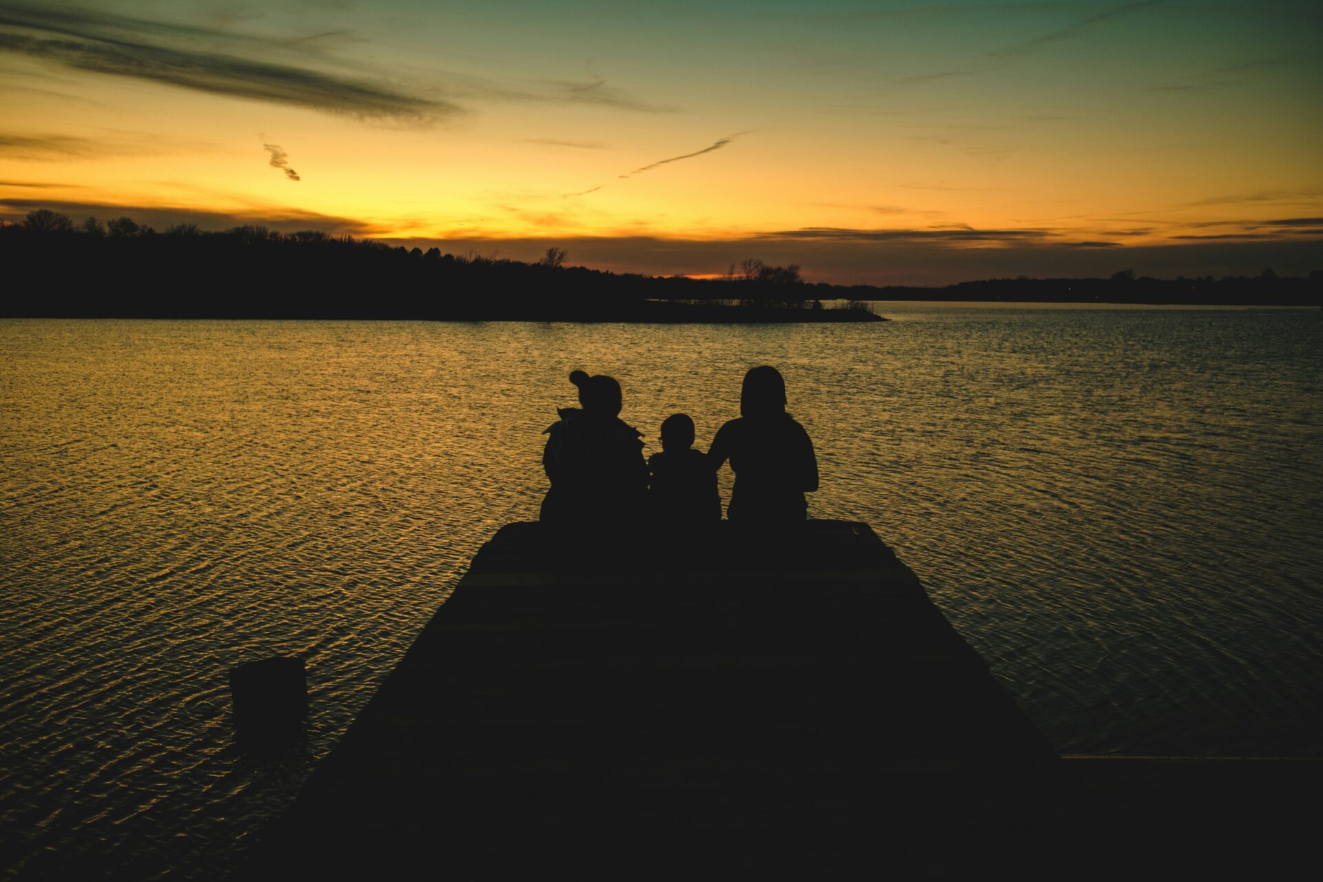 Familie sitzt gemeinsam an einem See bei Sonnenuntergang