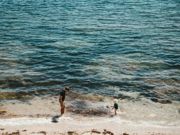 Vater beaufsichtigt ein Kind am Ufer eines Sees