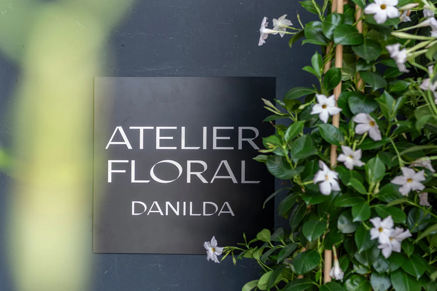 Eingangsschild von Atelier Floral Danilda mit blühender Pflanzenwand