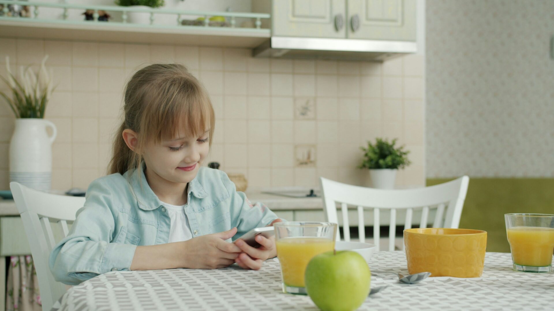 Mädchen sitzt am Esstisch und schaut auf ein Smartphone.
