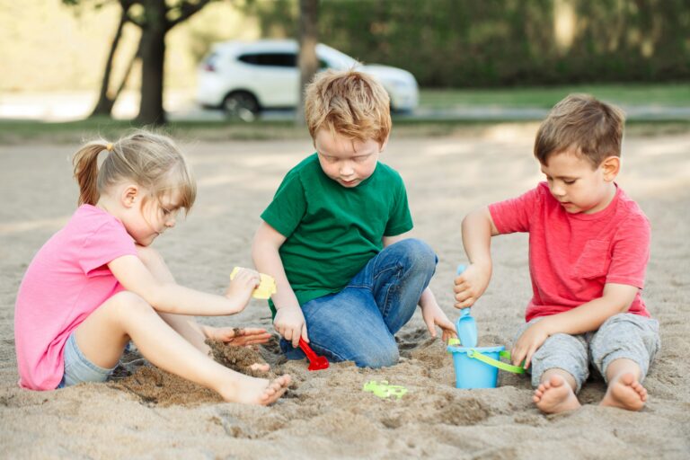 geschwisterstreit ferien, drei Geschwister spielen gemeinsam im Sandkasten