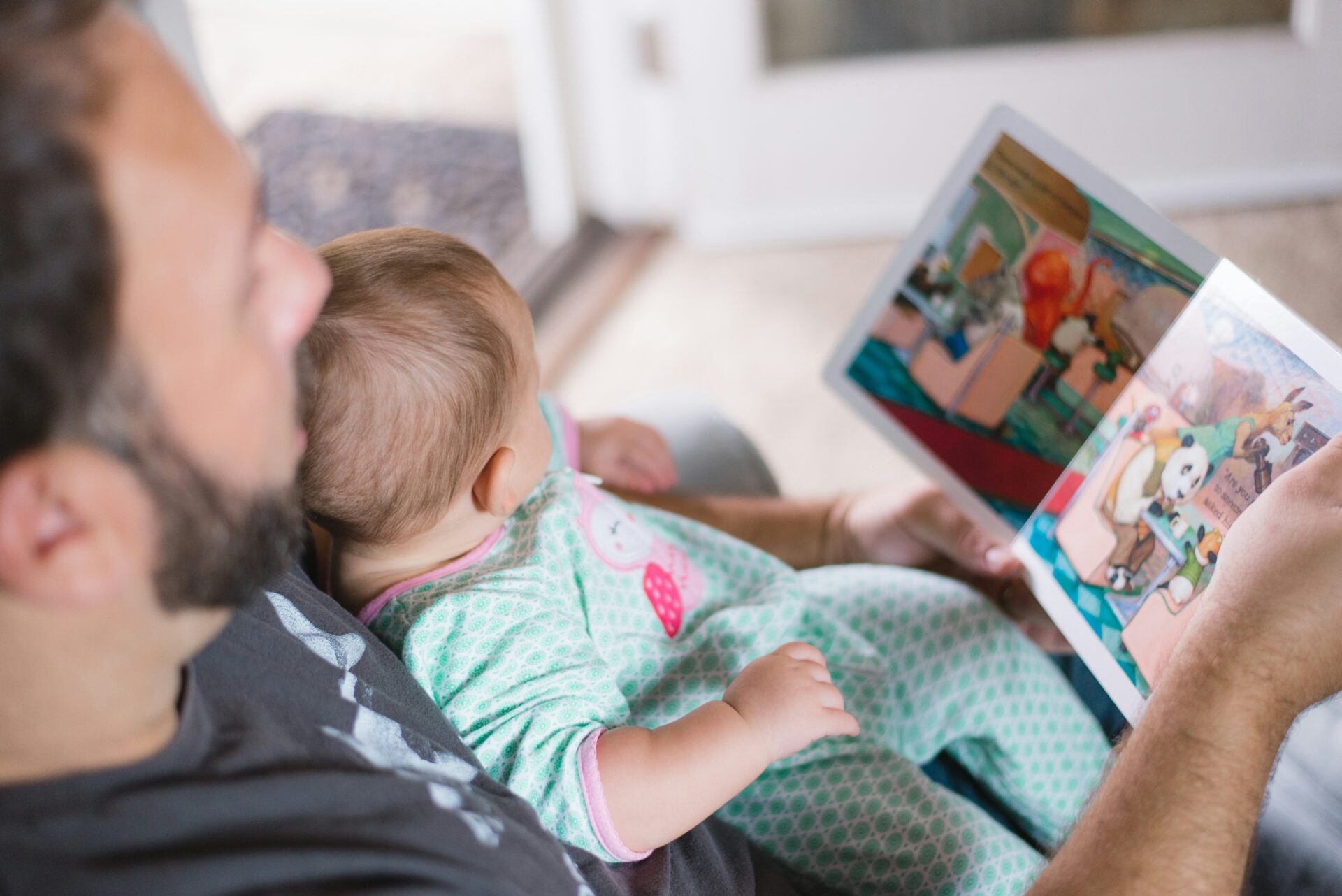 Zeit mit Kindern, Vater liest seinem Baby zu Hause ein Bilderbuch vor
