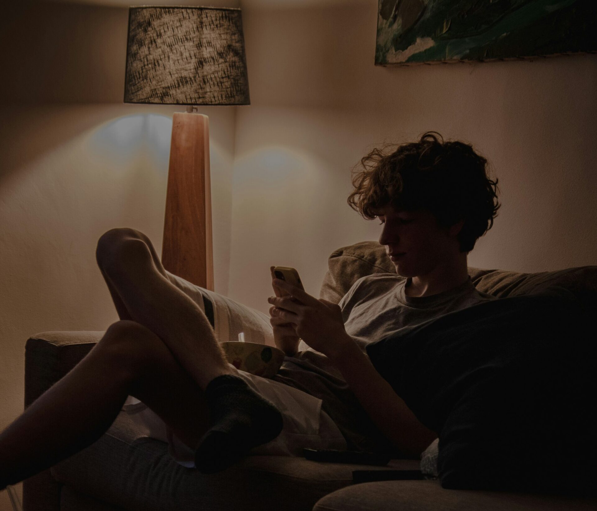 Jugendlicher sitzt abends auf dem Sofa und schaut auf sein Smartphone