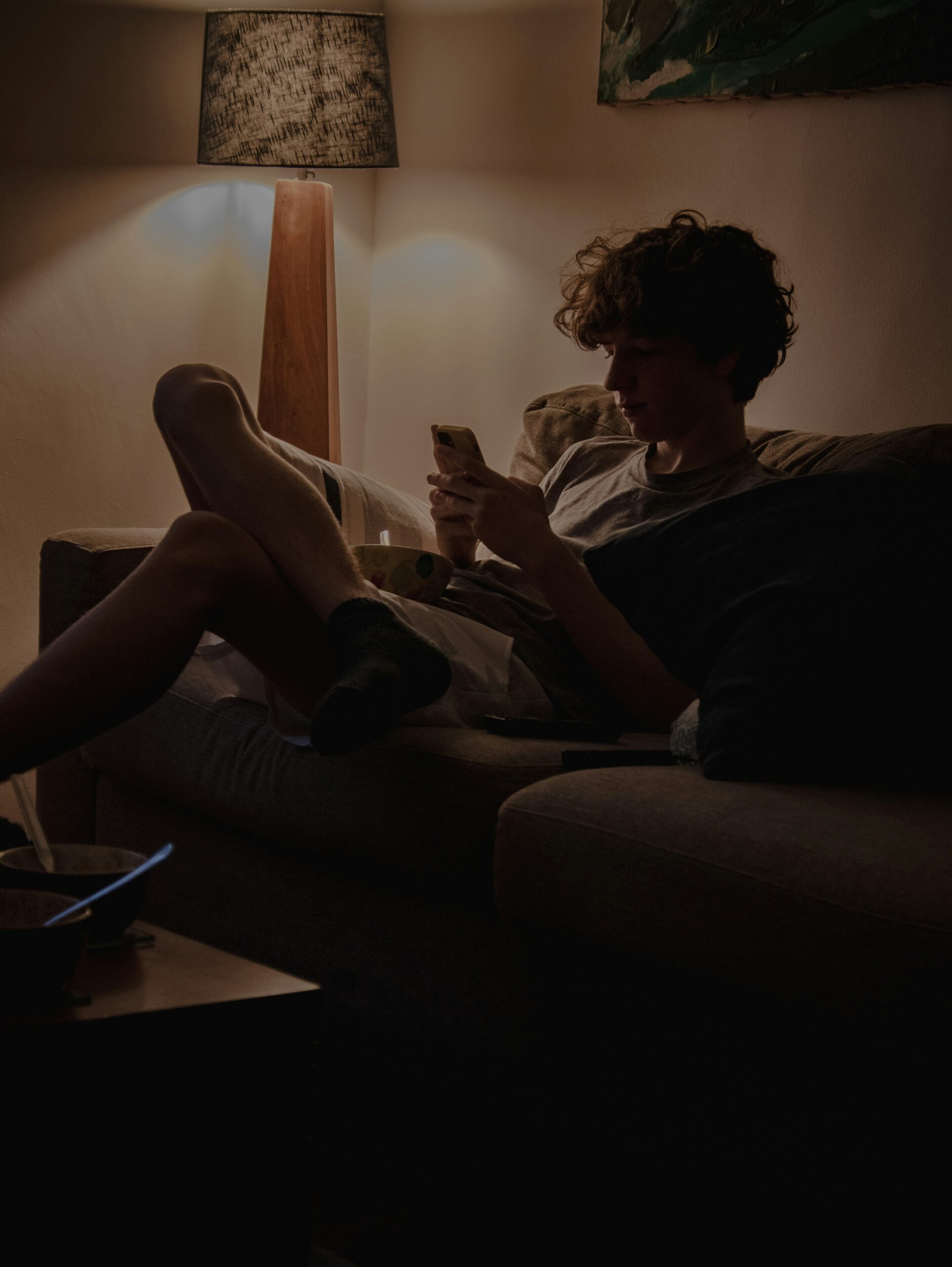 Jugendlicher sitzt abends auf dem Sofa und schaut auf sein Smartphone