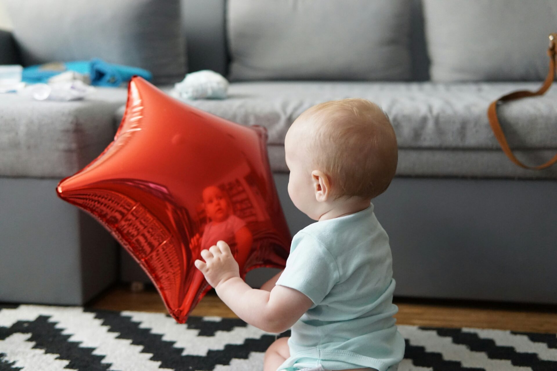 Baby sitzt im Wohnzimmer und hält einen roten Folienballon