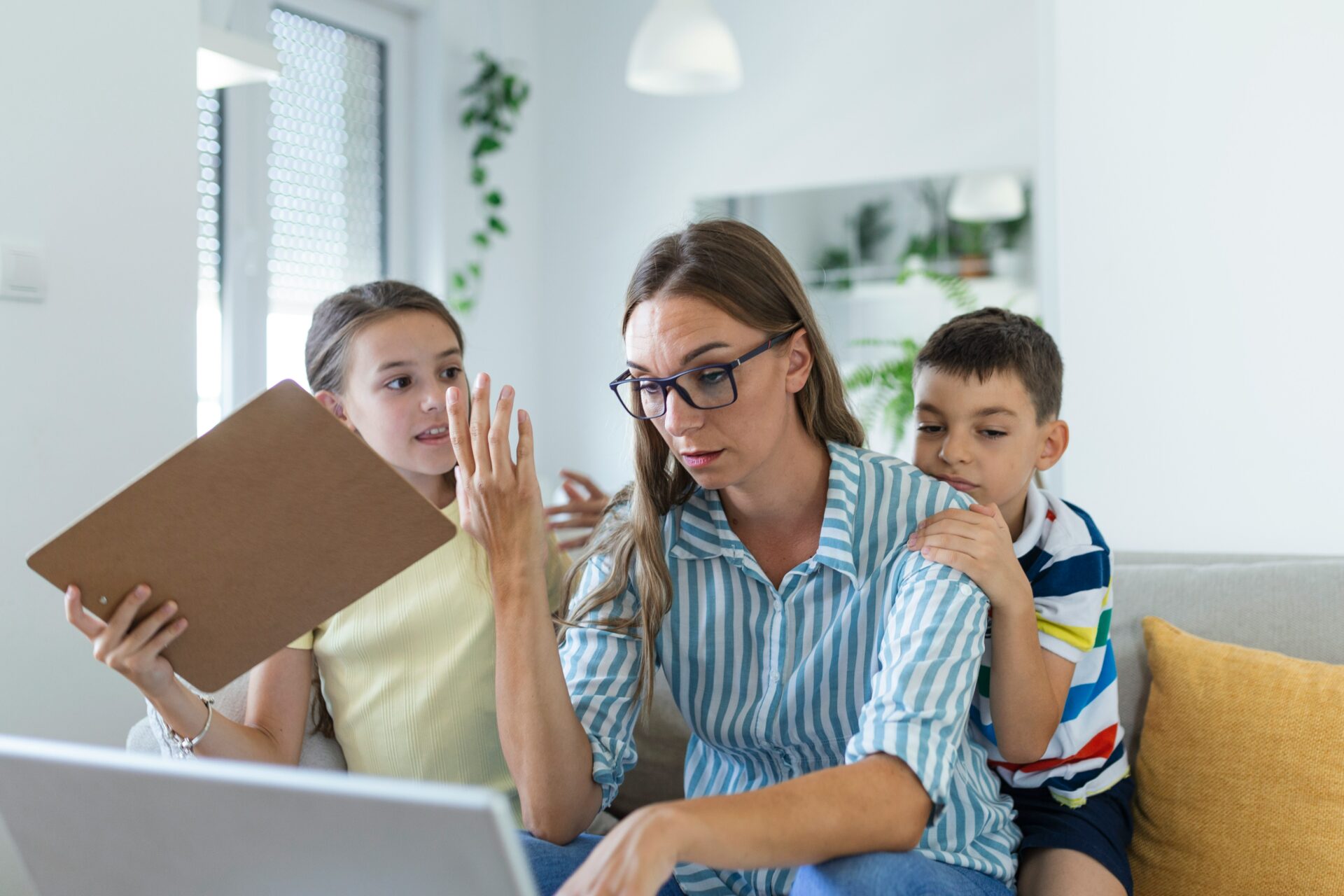 Mutter sitzt mit zwei Kindern vor einem Laptop zu Hause