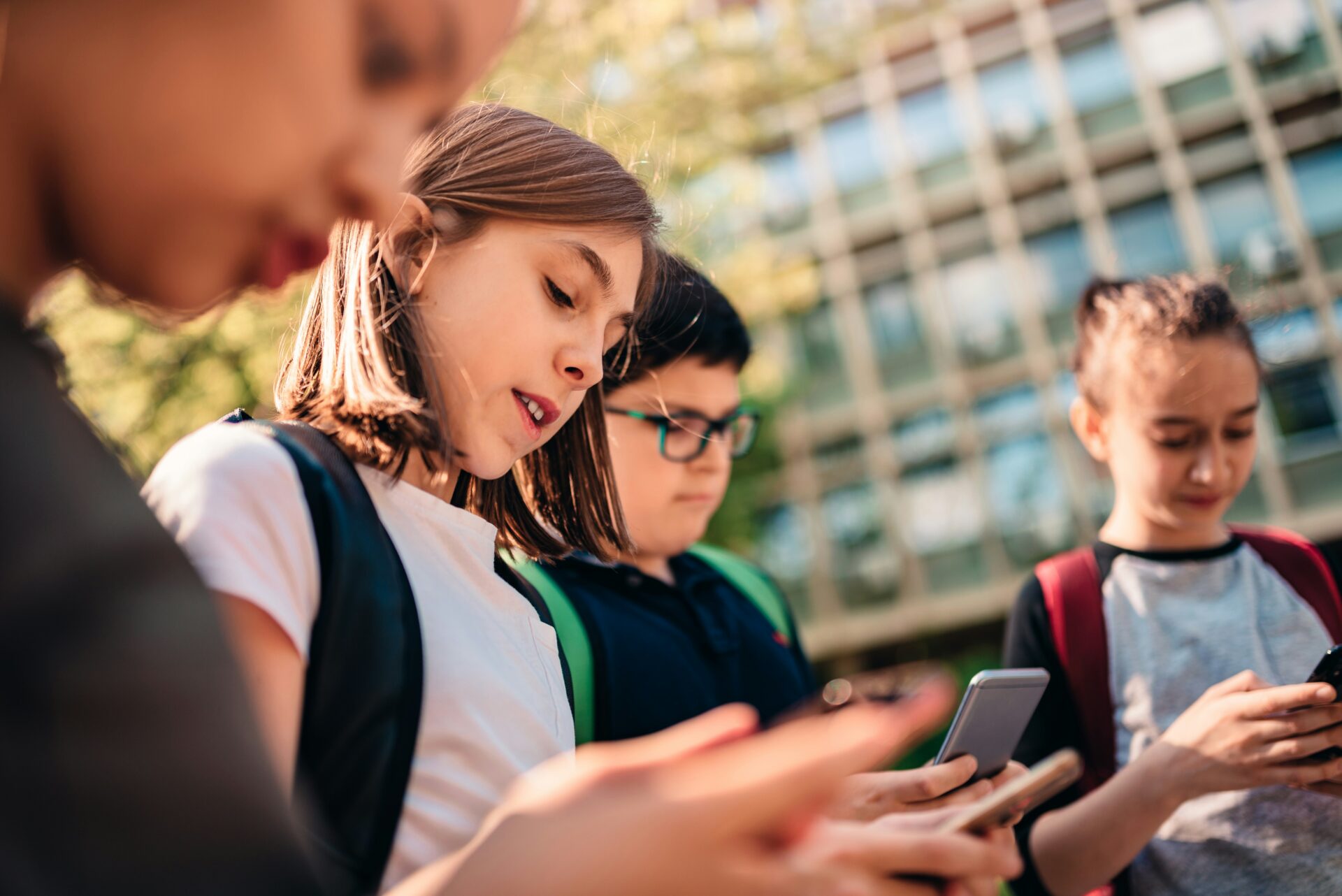 Gruppe von Schulkindern mit Smartphones vor einem Schulgebäude