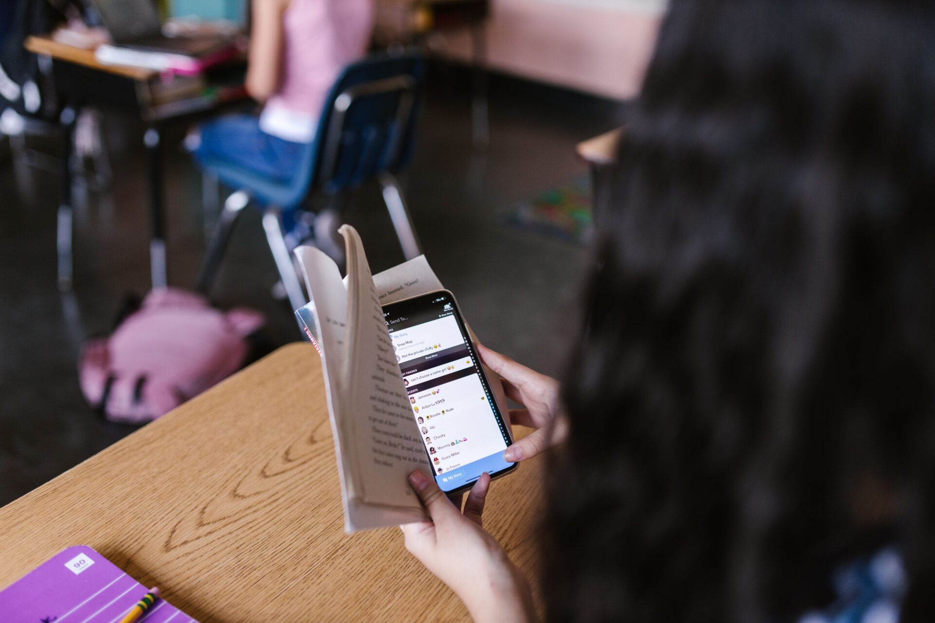 Schulkind nutzt ein Smartphone während es ein Buch in der Hand hält