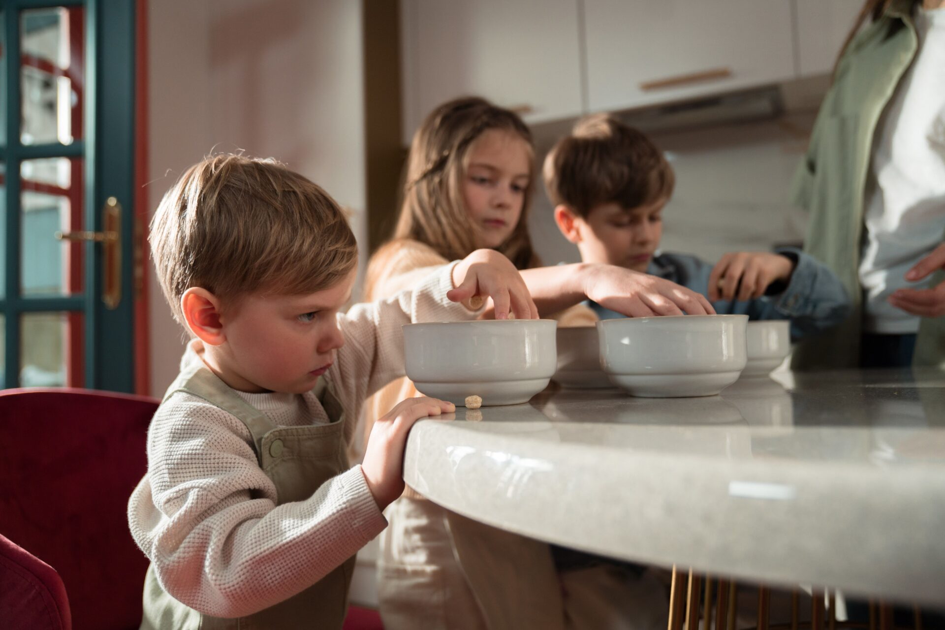 Drei Kinder stehen an einer Kücheninsel und greifen in Schüsseln
